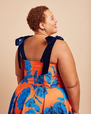 Woman wearing an orange and blue floral dress with bow straps on a beige background. This dress is the Ellington Strapless Dress sewing pattern from Cashmerette.