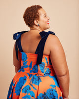 Woman wearing an orange and blue floral dress with bow straps on a beige background. This dress is the Ellington Strapless Dress sewing pattern from Cashmerette.