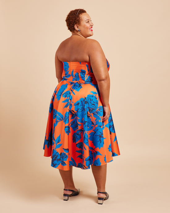 Woman wearing a strapless dress with blue and orange floral pattern on a beige background. This dress is the Ellington Strapless Dress sewing pattern from Cashmerette.