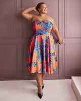 Woman wearing a strapless dress with blue floral pattern against a pink paneled wall. This dress is the Ellington Strapless Dress sewing pattern from Cashmerette.