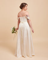 Woman in a white off-shoulder wedding dress holding a bouquet on a beige background. This dress is the Ellington Strapless Dress sewing pattern from Cashmerette.