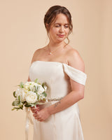 Woman in a white off-shoulder dress holding a bouquet against a beige background. This dress is the Ellington Strapless Dress sewing pattern from Cashmerette.