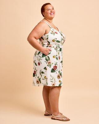A woman modeling a sleeveless white mini dress with a colorful floral and bird print, paired with metallic strappy sandals, against a solid beige studio background. This is the Wayland Dress sewing pattern from Cashmerette.