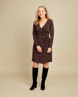 Woman wearing a patterned dress with long sleeves and knee-high boots on a beige background. This dress is the Appleton Wrap Dress sewing pattern from Cashmerette.