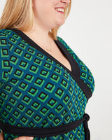 Woman wearing a green and black patterned dress with a plain background. This dress is the Appleton Wrap Dress sewing pattern from Cashmerette.