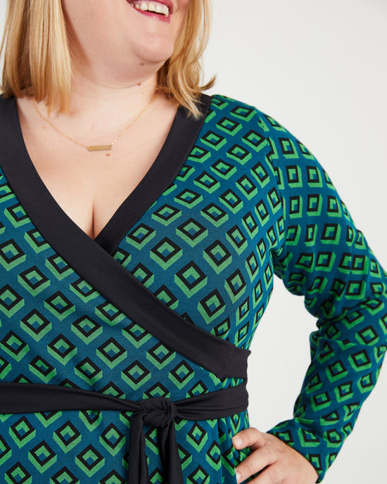 Woman wearing a green and black patterned dress with a black belt. This dress is the Appleton Wrap Dress sewing pattern from Cashmerette.