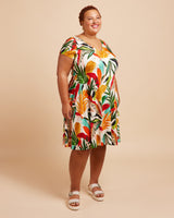 Woman wearing a colorful tropical print dress on a beige background