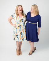 Two women standing side by side, one wearing a patterned dress and the other in a blue dress, on a plain background. This dress is the Turner Dress sewing pattern from Cashmerette.