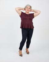 Woman wearing a burgundy top and black pants on a white background. This peplum top is the Rivermont Dress & Top sewing pattern from Cashmerette.