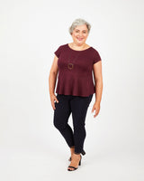 Woman wearing a burgundy top and black pants on a white background. This top is the Rivermont Dress & Top sewing pattern from Cashmerette.