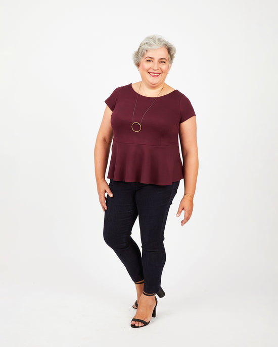 Woman wearing a burgundy top and black pants on a white background. This top is the Rivermont Dress & Top sewing pattern from Cashmerette.