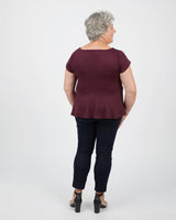 Person wearing a burgundy top and dark jeans on a white background. This peplum top is the Rivermont Dress & Top sewing pattern from Cashmerette.