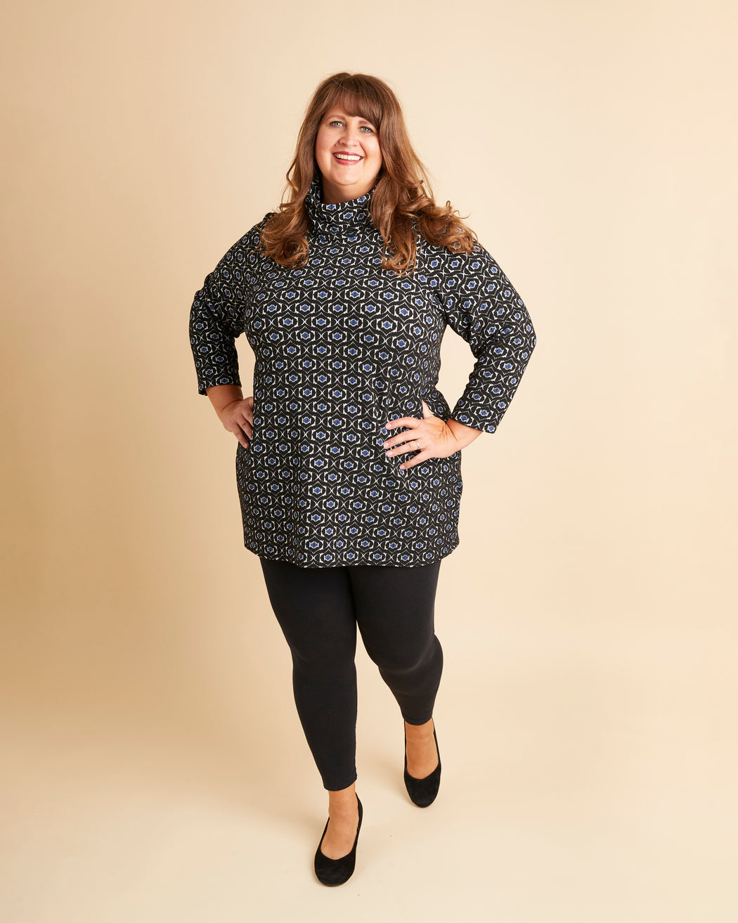 Woman wearing a patterned black and white dress with black leggings on a beige background. This is the Pembroke Dress & Tunic sewing pattern from Cashmerette.