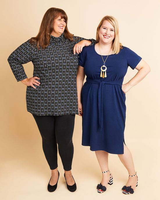 Two women standing side by side wearing black and blue dresses against a beige background. This is the Pembroke Dress & Tunic sewing pattern from Cashmerette.