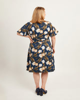 Woman wearing a floral dress with a plain background. This dress is the Alcott Dress sewing pattern from Cashmerette.