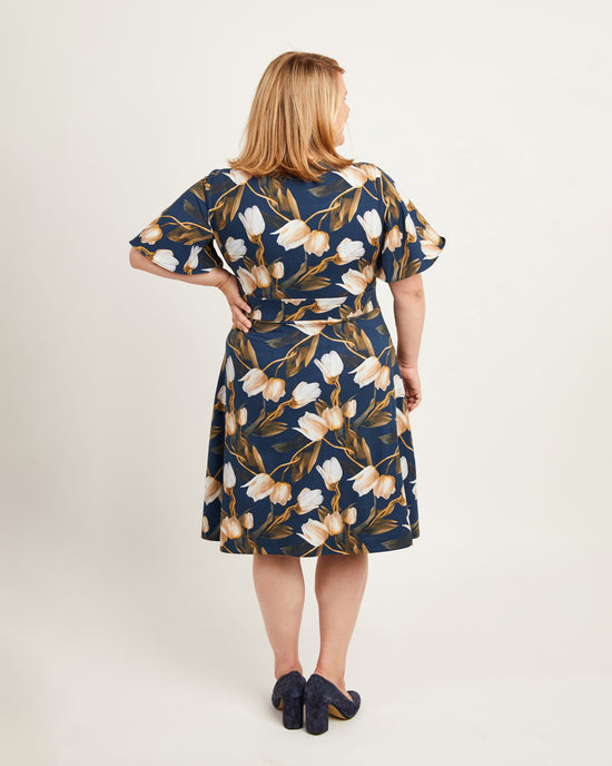 Woman wearing a floral dress with a plain background. This dress is the Alcott Dress sewing pattern from Cashmerette.