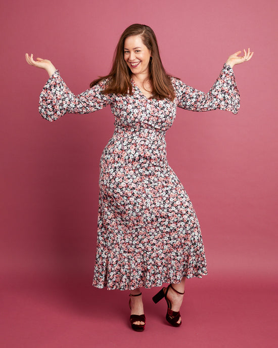 Woman wearing a floral dress against a pink background. This dress is the Alcott Dress sewing pattern from Cashmerette.