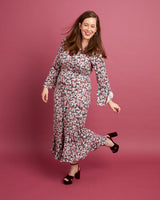 Woman wearing a floral dress on a pink background. This dress is the Alcott Dress sewing pattern from Cashmerette.