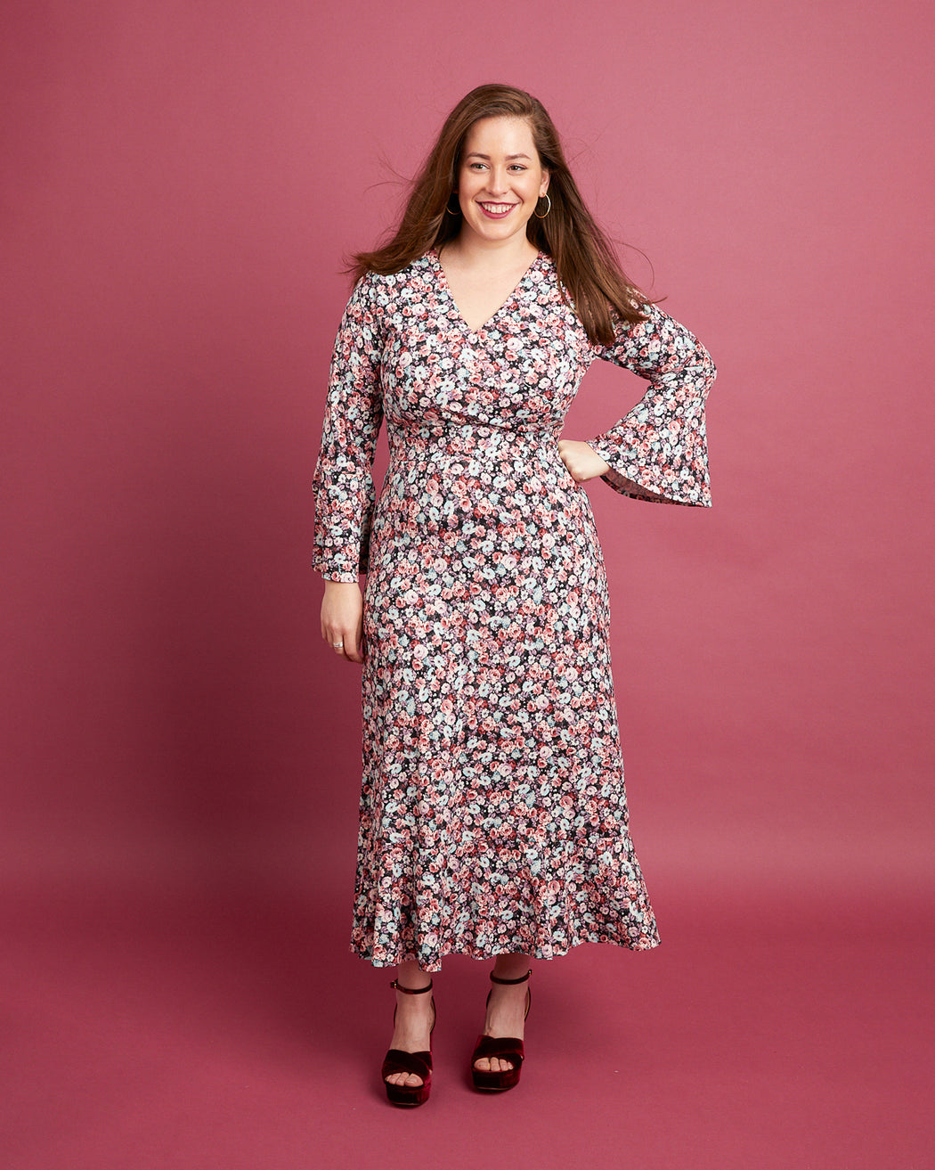 Woman wearing a floral dress against a pink background. This dress is the Alcott Dress sewing pattern from Cashmerette.