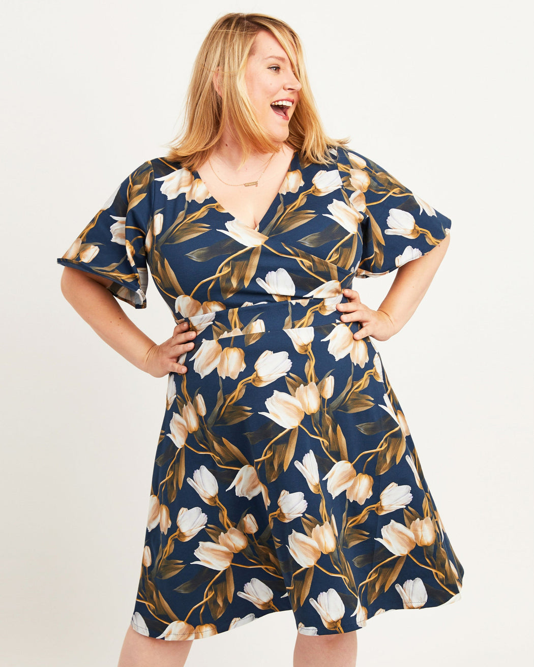 Woman wearing a navy dress with floral pattern on a white background. This dress is the Alcott Dress sewing pattern from Cashmerette.