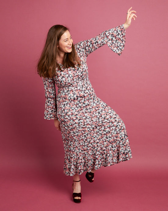 Woman in a floral dress posing against a pink background. This dress is the Alcott Dress sewing pattern from Cashmerette.