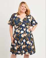 Woman wearing a floral dress on a plain background. This dress is the Alcott Dress sewing pattern from Cashmerette.