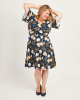 Woman wearing a floral dress on a white background. This dress is the Alcott Dress sewing pattern from Cashmerette.
