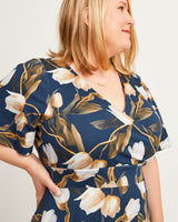 Woman wearing a navy blue dress with floral pattern on a plain background. This dress is the Alcott Dress sewing pattern from Cashmerette.