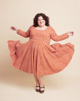 Woman wearing an orange patterned dress on a beige background. This is the Grafton Dress, Top & Skirt sewing pattern from Cashmerette.
