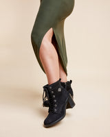 Black lace-up boots worn with a green dress on a beige background. This is the Grafton Dress, Top & Skirt sewing pattern from Cashmrette.