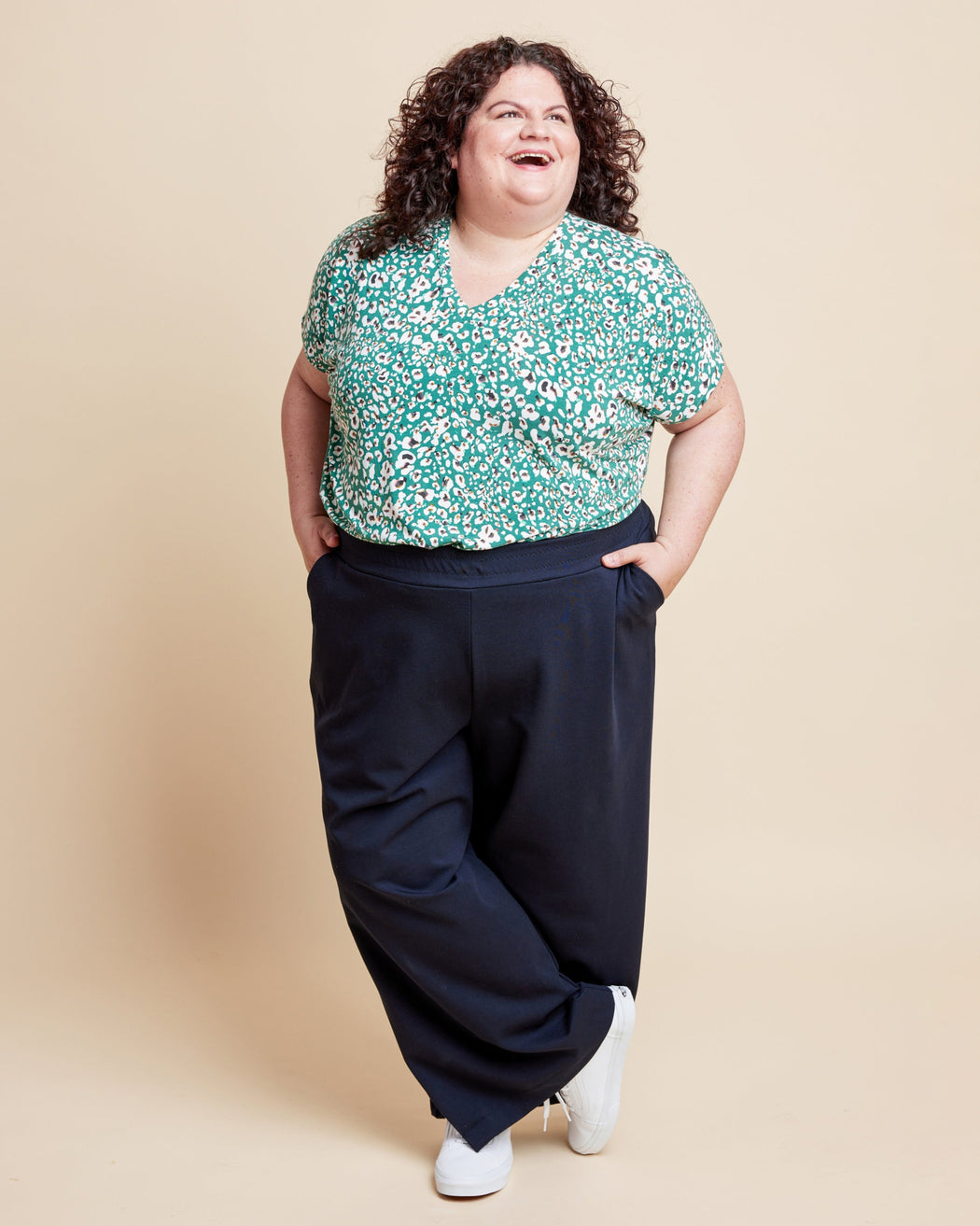 Woman wearing a floral top and dark pants on a beige background. This is the Grafton Dress, Top & Skirt sewing pattern from Cashmerette.