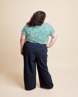 Person wearing a green floral top and navy pants on a beige background. This is the Grafton Dress, Top & Skirt sewing pattern from Cashmerette.