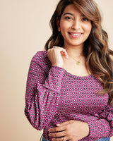 Woman wearing a patterned pink blouse against a beige background. This is the Grafton Dress, Top & Skirt sewing pattern from Cashmrette.