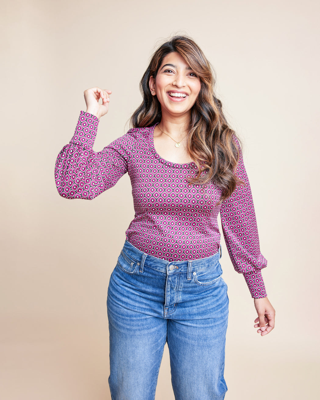 Woman wearing a patterned pink long-sleeve top and blue jeans against a beige background. This is the Grafton Dress, Top & Skirt sewing pattern from Cashmrette.