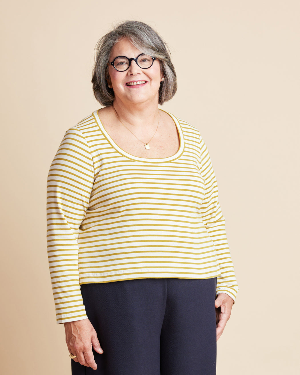 Woman wearing a yellow and white striped shirt against a beige background. This is the Grafton Dress, Top & Skirt sewing pattern from Cashmerette.