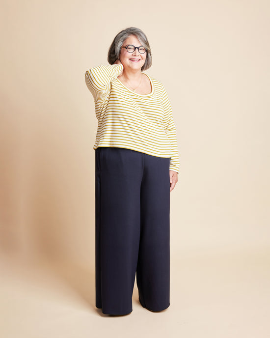 Woman wearing a yellow striped shirt and navy pants against a beige background. This is the Grafton Dress, Top & Skirt sewing pattern from Cashmerette.