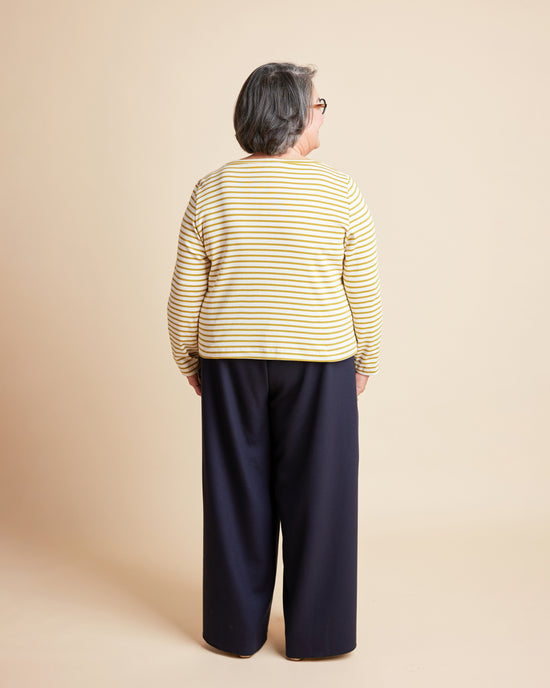 Person wearing a yellow striped shirt and navy pants on a beige background. This is the Grafton Dress, Top & Skirt sewing pattern from Cashmerette.