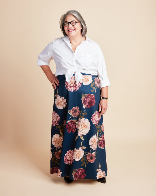 Woman wearing a white blouse and floral skirt on a beige background. This is the Grafton Dress, Top & Skirt sewing pattern from Cashmerette.