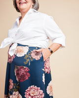 Woman wearing a white blouse and floral skirt on a beige background. This is the Grafton Dress, Top & Skirt sewing pattern from Cashmerette.