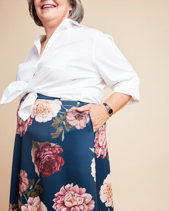 Woman wearing a white blouse and floral skirt on a beige background. This is the Grafton Dress, Top & Skirt sewing pattern from Cashmerette.