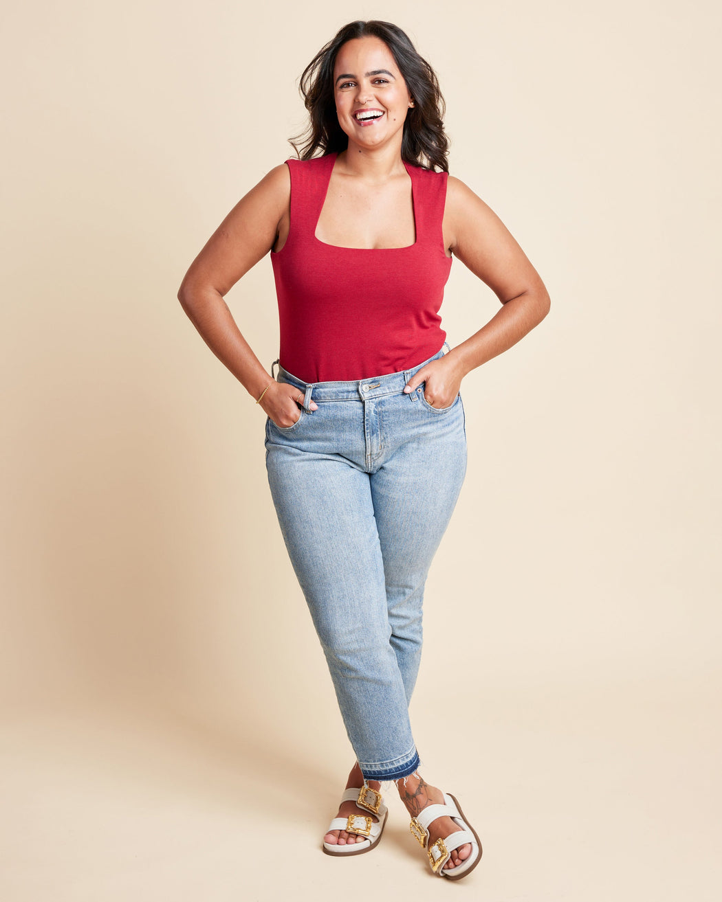 Woman wearing a red tank top and blue jeans against a beige background. This is the Grafton Dress, Top & Skirt sewing pattern from Cashmrette.