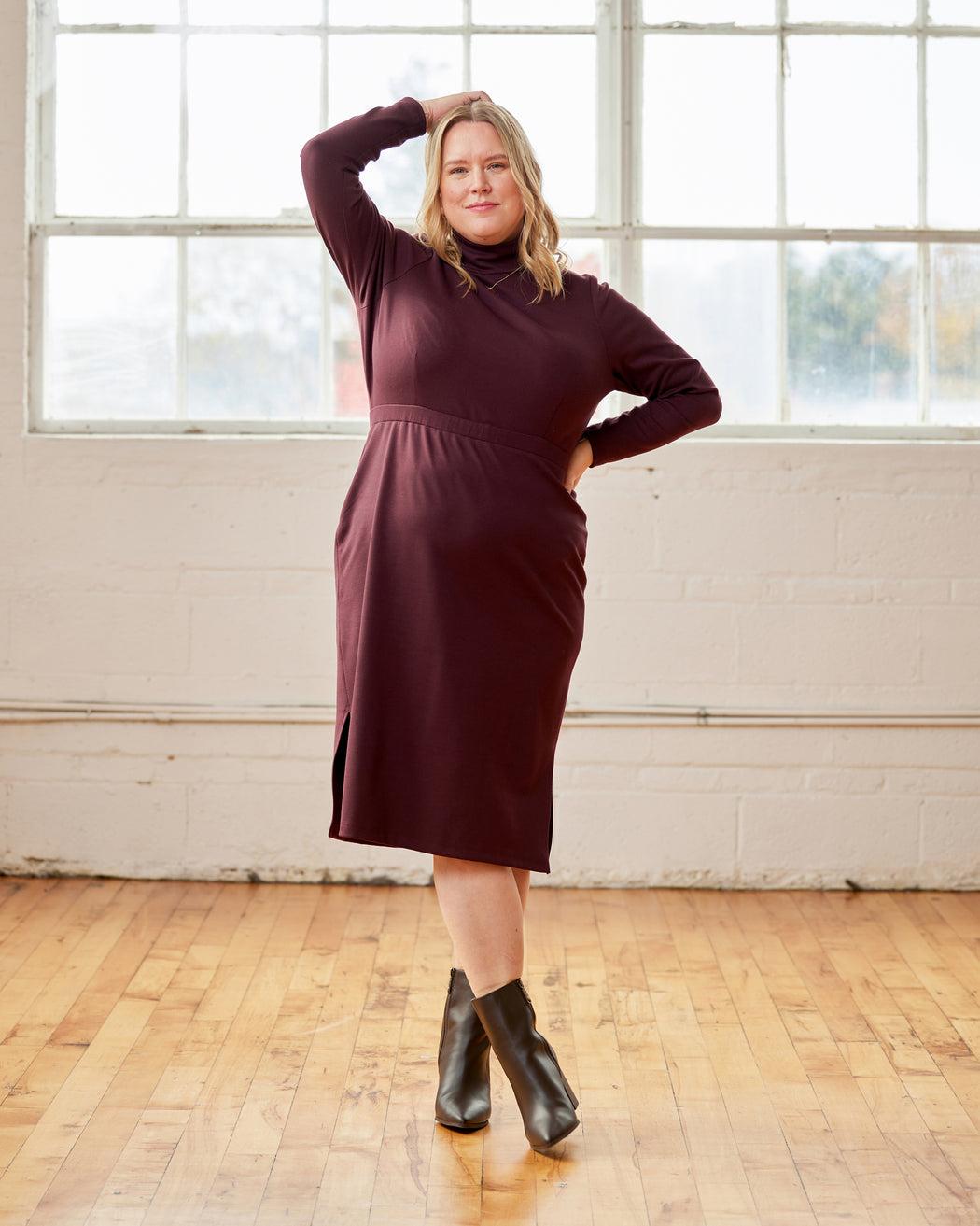 Woman wearing a burgundy dress standing in a room with large windows and wooden floor. This is the Grafton Dress, Top & Skirt sewing pattern from Cashmerette.
