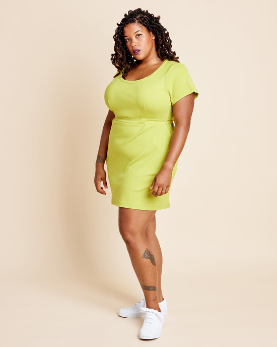Woman wearing a bright green dress against a beige background. This is the Grafton Dress, Top & Skirt sewing pattern from Cashmerette.