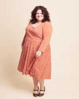 Woman wearing an orange dress with a pattern on a beige background. This is the Grafton Dress, Top & Skirt sewing pattern from Cashmerette.