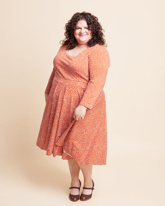 Woman wearing an orange dress with a pattern on a beige background. This is the Grafton Dress, Top & Skirt sewing pattern from Cashmerette.
