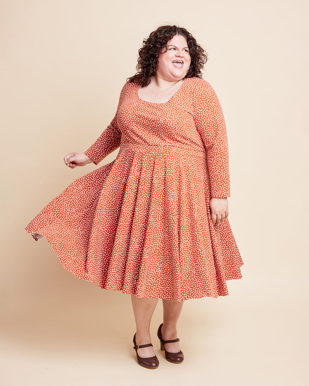 Woman wearing an orange patterned dress against a beige background. This is the Grafton Dress, Top & Skirt sewing pattern from Cashmerette.