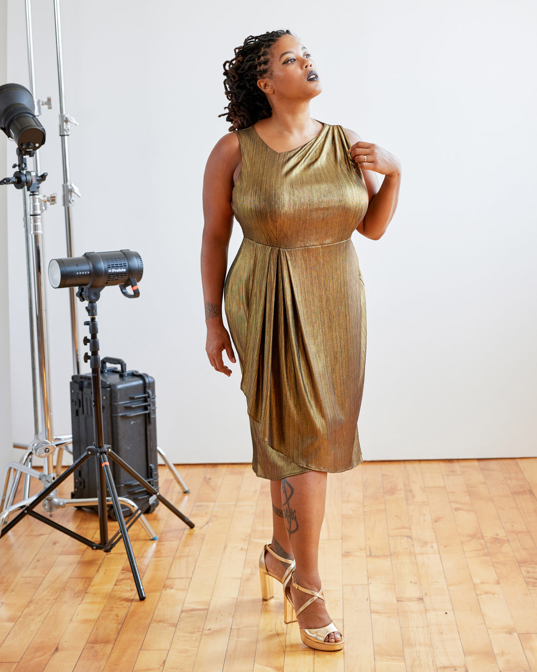 Woman in a gold dress standing in a studio setting with photography equipment. This dress is the Dewey Dress sewing pattern from Cashmerette.