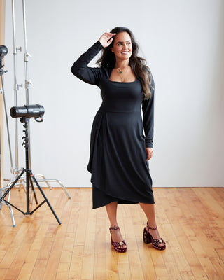 Woman wearing a black dress standing in a studio setting with photography equipment. This dress is the Dewey Dress sewing pattern from Cashmerette.