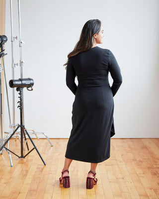 Woman in a black dress standing in a photo studio with equipment. This dress is the Dewey Dress sewing pattern from Cashmerette.
