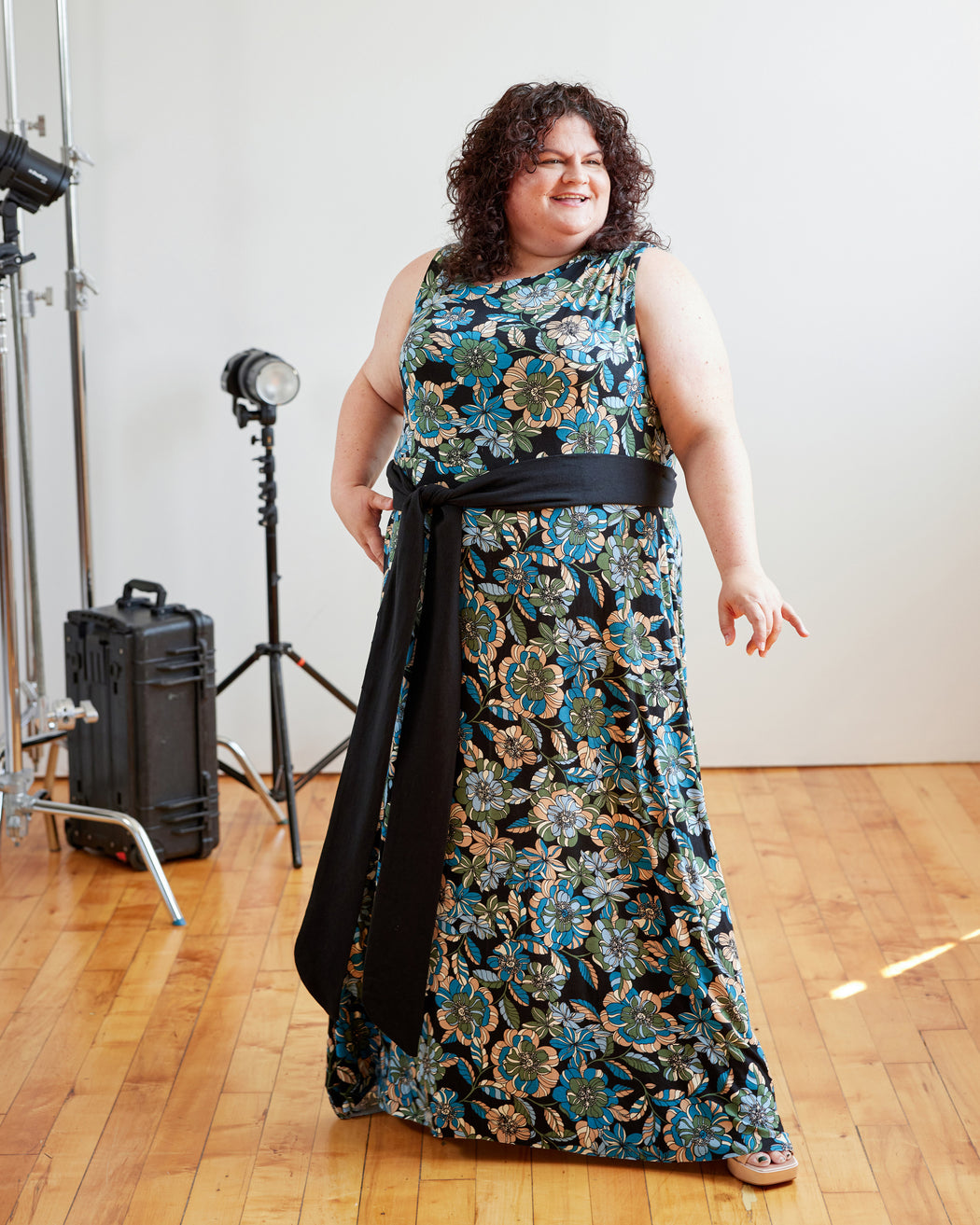 Woman wearing a floral dress in a studio setting with photography equipment. This dress is the Dewey Dress sewing pattern from Cashmerette.